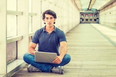 New York'ta okuyan genç Amerikan Koleji Öğrencisi, mavi kısa kollu kısa, kot pantolon, spor ayakkabı, kampüste kapalı geçit içinde yerde bacaklı oturma, dizüstü bilgisayar üzerinde çalışan giyiyor.