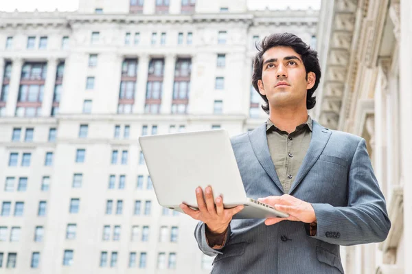 Way to success. Young Mix Race American College Student studying in New York City, wearing dark blue jacket, standing outside old style office building, working on laptop computer, looking, thinking