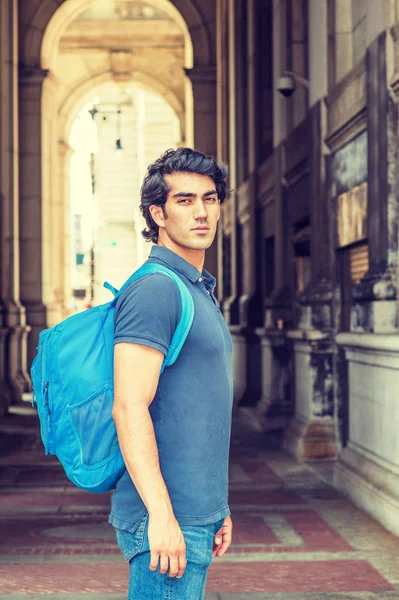 Back to School. Mix Race American college student wearing blue short sleeve shirt, jeans, shoulder carrying back bag, standing on street on campus in New York City, coming back from summer vacatio