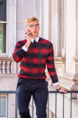 Genç sarışın Amerikan üniversite öğrencisi desenli kırmızı giyiyor, siyah örgü kazak, gözlük, New York'ta vintage ofis binasında korkuluk tarafından oturan, cep telefonu konuşuyor