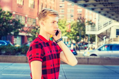 Genç sarışın Amerikan Adam kırmızı desenli Polo gömlek giyiyor, New York'ta işlek sokakta yürürken, cep telefonu konuşuyor. Arabalar, arka planda sokak köprüsü