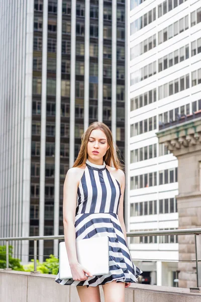 ヨーロッパの大学生の旅行 ニューヨークでの勉強 ノースリーブ 白のストライプのドレスを着て ラップトップコンピュータを保持し 高い建物で通りを歩いて 見下ろす 疲れた — ストック写真