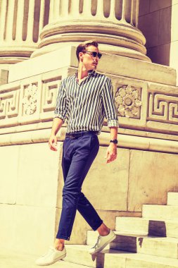 Siyah giyen genç Amerikalı adam, beyaz çizgili, uzun kollu gömlek, mavi pantolon, beyaz spor ayakkabı, güneş gözlüğü, New York'ta ofis binası dışında merdivenlerden aşağı yürüme, güçlü güneş altında, bak görünümlü