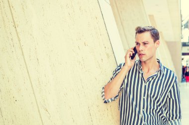 New York'ta dışarıda dinlenen genç Amerikalı adam. Siyah beyaz çizgili, uzun kollu gömlek giyen genç yakışıklı adam, ofis binası dışında sütun karşı duran, kaşlarını çattı, cep telefonu konuşuyor