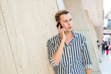 New York'ta dışarıda dinlenen genç Amerikalı adam. Siyah beyaz çizgili, uzun kollu gömlek giyen genç yakışıklı adam, ofis binası dışında sütun karşı duran, cep telefonukonuşuyor