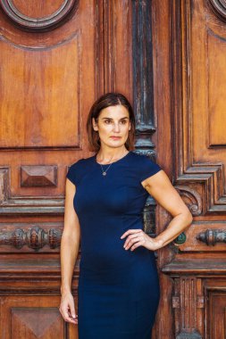 New York 'ta çalışan yerli bir iş kadını. Mavi kısa kollu bir elbise giyen genç, güzel bayan öğretmen, kahverengi klasik ofis kapısının yanında duruyor, elleri kalçalarında, kendinden emin bir şekilde ileriye bakıyor.