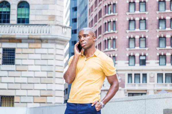 New York 'ta genç Afro-Amerikan erkek sokak modası. Sarı kısa kollu gömlekli, kısa saçlı genç bir üniversite öğrencisi ofis binasının önünde duruyor, cep telefonuyla konuşuyor.