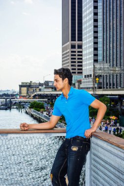 Yağmurdan sonra bulutlu bir gün - karanlık, ıslak, kumlu bir his. Doğu Hintli Amerikalı genç New York 'un dışında mavi tişört giyiyor, siyah yırtık moda kot pantolon giyiyor, East River' ın yanında duruyor, üzgün.