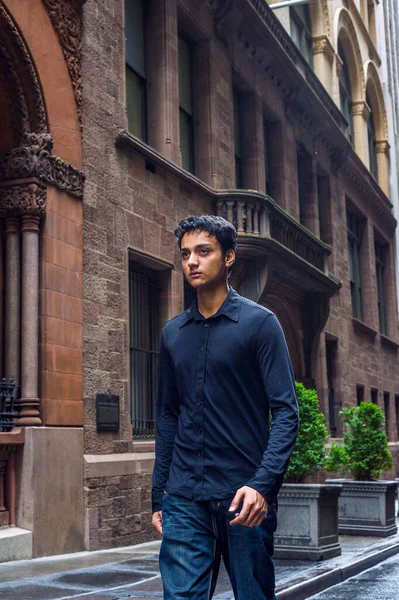 Raining day - wet, drizzle, grainy feel. Lonely East Indian American teenager wearing black long sleeve shirt,  broken fashionable jeans, walking on narrow old street in Manhattan of New York City