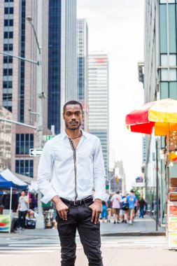 Beyaz uzun kollu gömlekli, siyah pantolonlu, New York 'un Manhattan şehir merkezinde modern yüksek binalarla caddede dikilen sakallı genç Afrikalı Amerikalı.