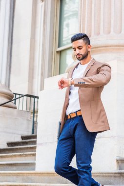 New York 'ta sakallı, kahverengi ceketli, mavi pantolonlu, kollarını kaldırmış, kol saatine bakıyor, ofis binasından merdivenlerden aşağı iniyor.