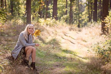 Ormanın içinden güneşli bir sonbahar gününde yürüyen bir genç, sarışın kadın.