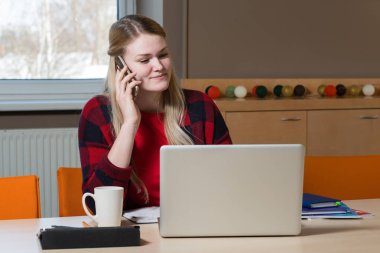 Bir dizüstü bilgisayar oturma ve bir cep telefonu üzerinde konuşurken sarışın bir kadın.