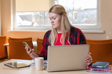 Gülümseyen çay içme ve çalışma bir laptop oturan sarışın kadın.