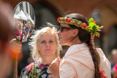 Riga, Letonya - 22 Haziran 2018: yaz gündönümü Pazar. Kadın aynaya bakar ve çiçek taç çalışır.