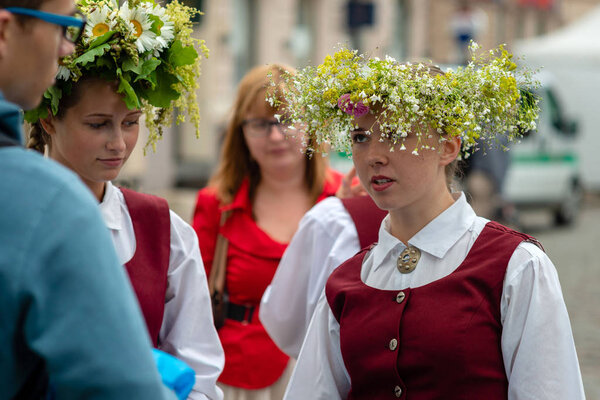 RIGA, LATVIA - JUNE 22, 2018: Summer solstice market. A young woman dressed in a national costume talking to her friends.