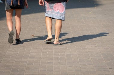Güneşli bir günde, birkaç kişi kaldırım boyunca yürümek. İnsan gölgeler kaldırımda görülebilir. Arkadan görüntülemek.