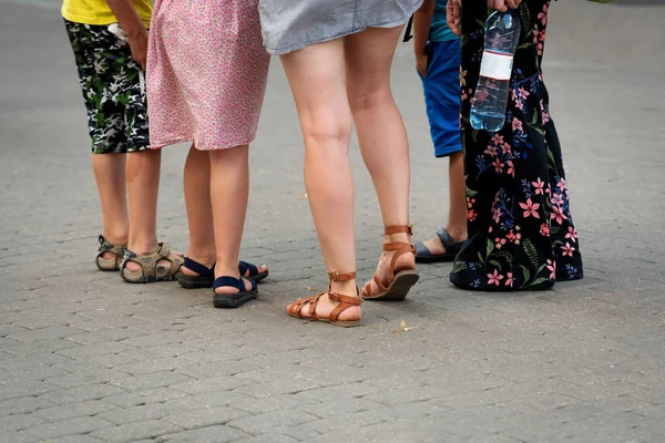 On a hot summer day, a group of people stands on the street. Only legs visible.