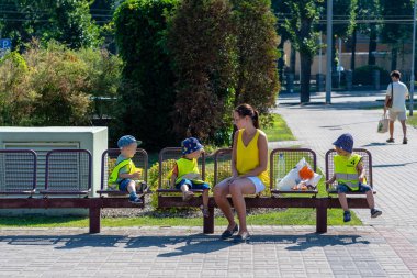 Riga, Letonya - 27 Temmuz 2018: Kadın ve çocuk parkta bir bankta oturan sarı reflektif yelekler.