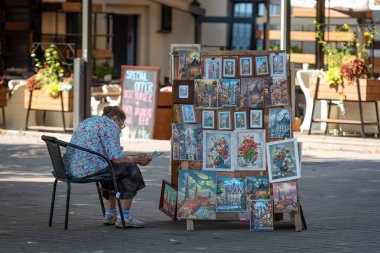 Riga, Letonya - 31 Temmuz 2018: Hediyelik eşya satıcı sokakta bir sandalyeye oturur ve bir kitap okumak.