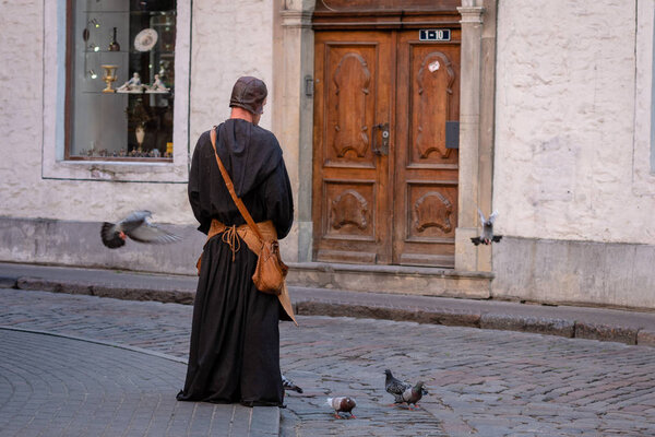 RIGA, LATVIA - JULY 31, 2018: Man in medieval clothes in the old town on the street feeds the pigeons.