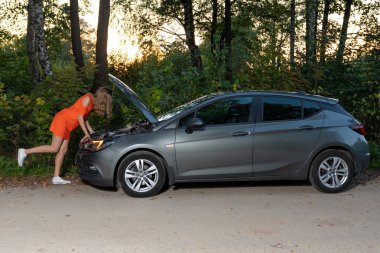 Genç bir kız kırık bir araba standları ve motora görünüyor, nasıl tamir anlamıyor