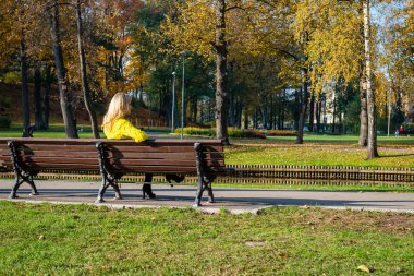 Bir parkta bir bankta oturan genç, güzel, sarışın bir bayan.