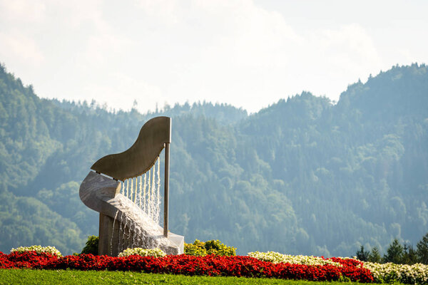 The harp fountain in Ossiach, Austria. Forest and mountains in the background.