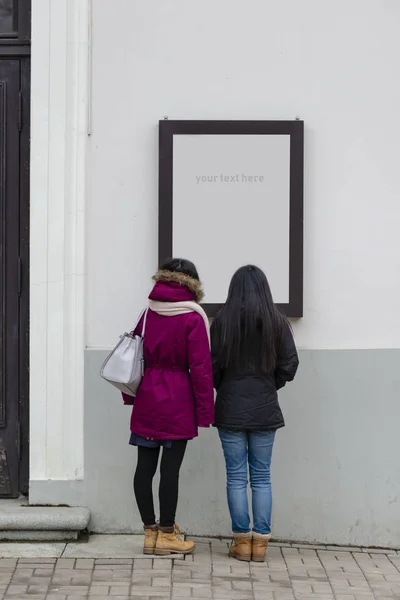 Dos mujeres se paran en el cartel y leen el texto. Vista desde atrás. Concepto publicitario . —  Fotos de Stock