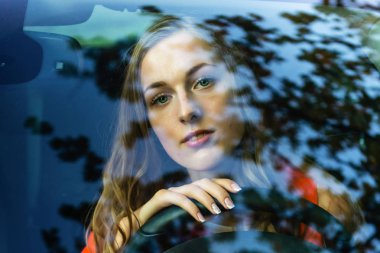 Uzun saçlı Genç, güzel bir kadın araba direksiyon başında oturur ve dreamingly ön cam parlama ile izledim.