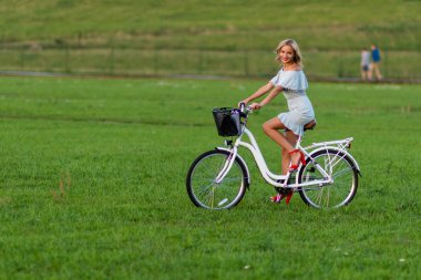 Yumuşak odak fotoğraf. Genç, güzel bir sarışın kadın yeşil bir çayırda beyaz bir bisiklet ile.