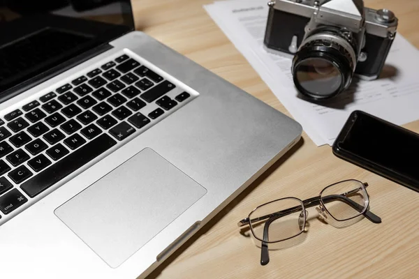 Wooden photographer desk table with camera, laptop, smartphone and eyeglasses - Image