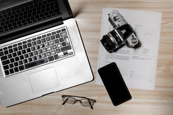 Wooden photographer desk table with camera, laptop, smartphone and eyeglasses. Top view, flat lay. - Image