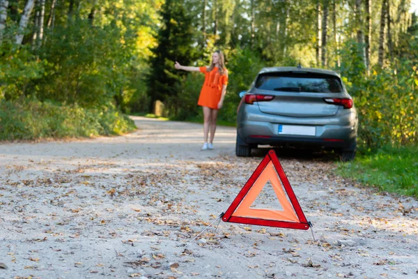 Stressige junge Autofahrerin trampt und stoppt Autos, bittet um Hilfe, weil sie Probleme mit kaputten Autos hat, warnt Autofahrer mit rotem Dreieck vor Anhalten. (Selektiver Fokus) — Stockfoto