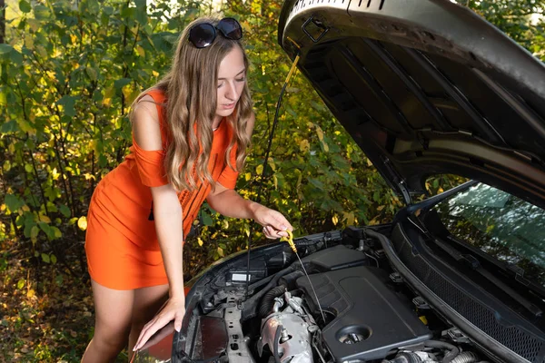 Probleme mit dem Auto. Die Frau überprüft den Ölstand des Motors. — Stockfoto