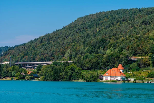 Worthersee, Αυστρία - 08 Αυγούστου 2018: Μεγάλο τοπίο από το σκάφος της γραμμής ακτή η λίμνη, όμορφα κτίρια, βουνά, δάση, αυτοκινητόδρομοι. — Φωτογραφία Αρχείου