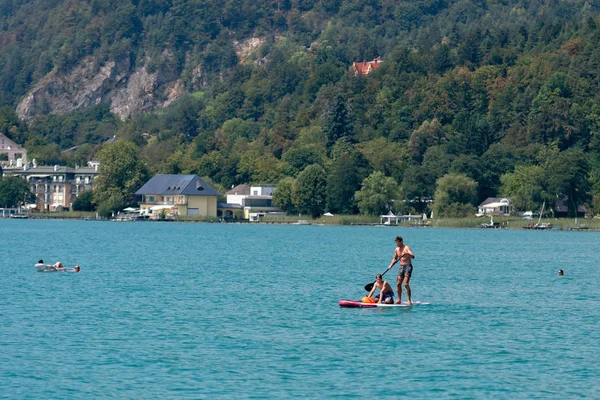 WORTHERSEE, AUSTRIA - 08 de agosto de 2018: Vista desde el barco hasta el lago y la costa. Residentes locales y turistas nadan, conducidos por lanchas y utilizan otras formas de recreación acuática . — Foto de Stock