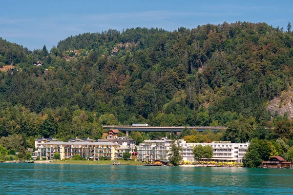 WORTHERSEE, AUSTRIA - 08 AGOSTO 2018: Grandes paisajes desde el barco hasta la orilla del lago, hermosos edificios, montañas, bosques, carreteras . — Foto de Stock