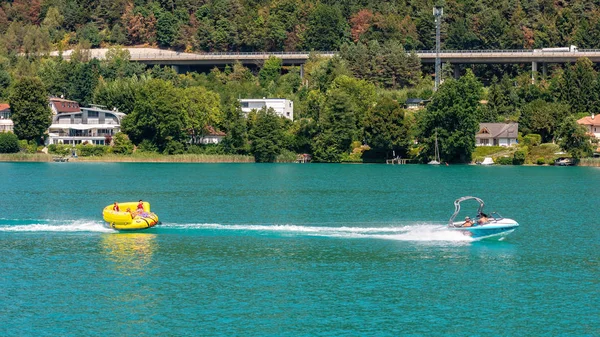 Worthersee, Австрія - 08 серпня 2018 роки: Щасливий молодих людей, на Надувні атракціони, диск позаду моторному човні по озеру. — стокове фото