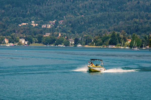 WORTHERSEE, AUSTRIA - 08 de agosto de 2018: Vista desde el barco hasta el lago y la costa. Residentes locales y turistas nadan, conducidos por lanchas y utilizan otras formas de recreación acuática . — Foto de Stock