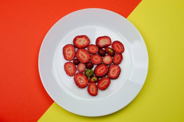 Yaratıcı Sevgililer Günü romantik konsept kompozisyon düz turuncu ve sarı arka plan üzerinde izole beyaz bir tabak üzerinde kalp çilek ile üst görünümü yatıyordu. 