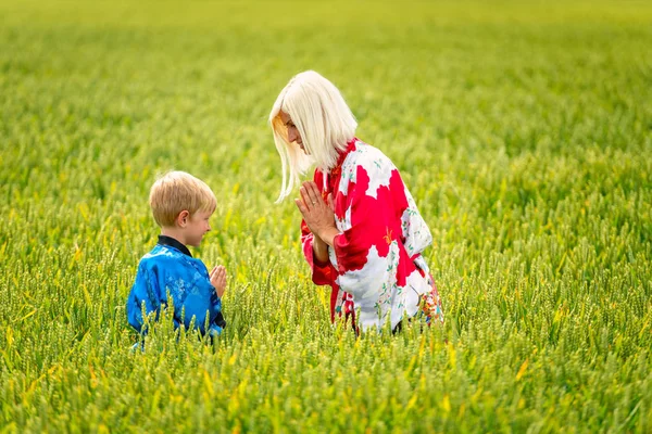 Una mujer rubia con un hijo, vestida con kimono, en un campo de cereales . —  Fotos de Stock