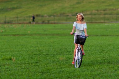 Yumuşak odak fotoğraf. Genç, güzel bir sarışın kadın yeşil bir çayırda beyaz bir bisiklet ile.