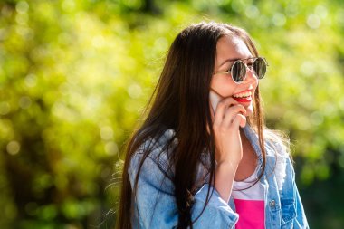 Güzel, duygusal, güneş gözlüklü genç bir kadın telefonda konuşuyor. Yumuşak arka plan. Kopyalama alanı.