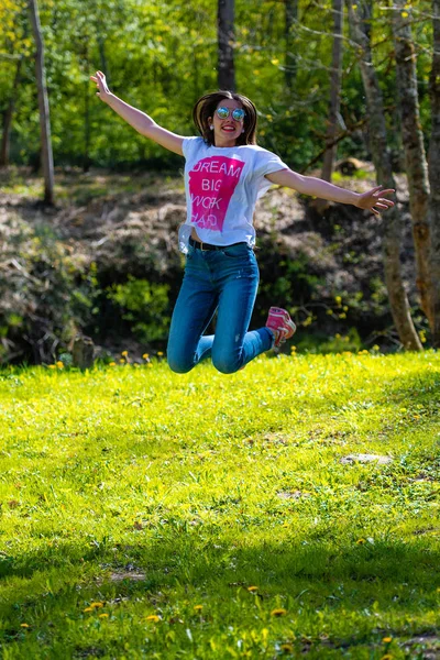 DOBELE, Letonia, - 7 de mayo de 2019: Joven mujer atractiva en gafas de sol saltando en el prado . — Foto de Stock