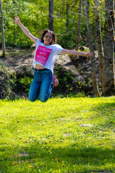 DOBELE, Letonia, - 7 de mayo de 2019: Joven mujer atractiva en gafas de sol saltando en el prado . — Foto de Stock
