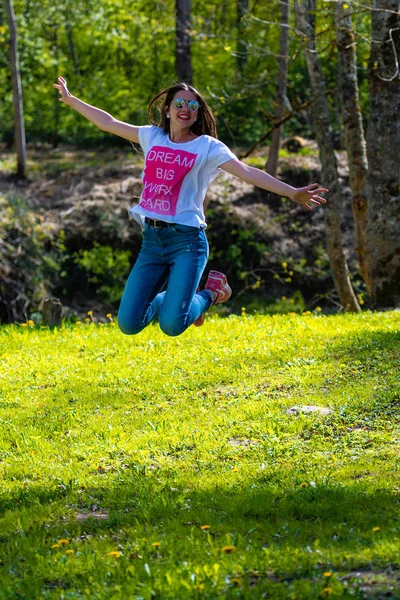 DOBELE, Letonia, - 7 de mayo de 2019: Joven mujer atractiva en gafas de sol saltando en el prado . — Foto de Stock