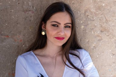 Güneşli bir günde eski bir taş duvarın yanında gülümseyen genç bir kadın.