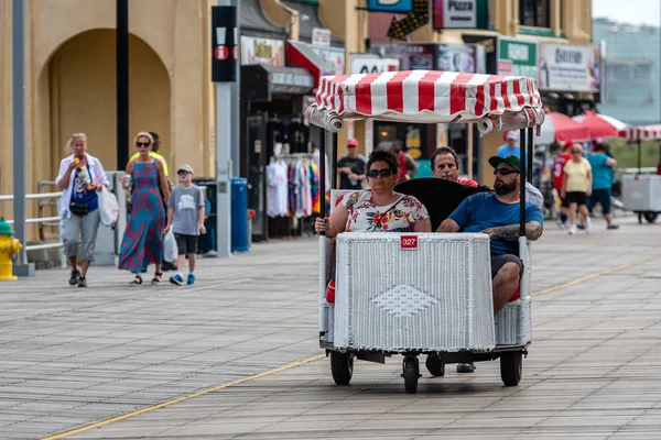 ATLANTIC CITY, NEW JERSEY - JUNE 18, 2019: A pedicab pushes his customers past the Boardwalk lined with restaurants, shop and casino. — Stock Photo, Image