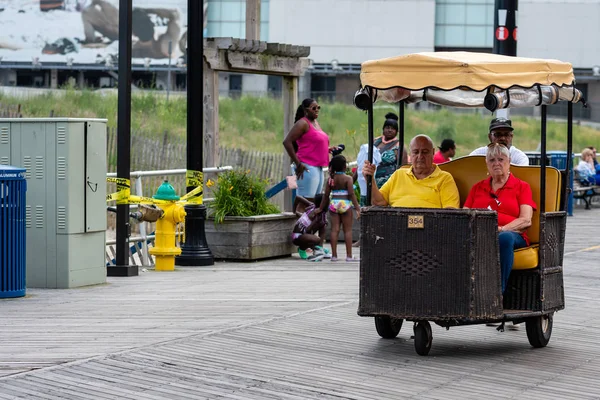 CIUDAD DEL ATLÁNTICO, NUEVA JERSEY - 18 DE JUNIO DE 2019: Un pedicab empuja a sus clientes más allá del paseo marítimo lleno de restaurantes, tiendas y casinos . — Foto de Stock